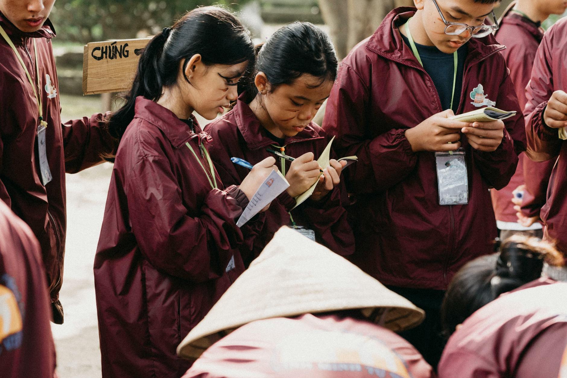 Uczniowie w bordowych marynarkach notują podczas lekcji w plenerze